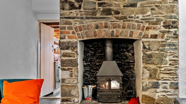 A stone fireplace with a modern stove, a teal sofa with an orange cushion, and a red bag on the floor.