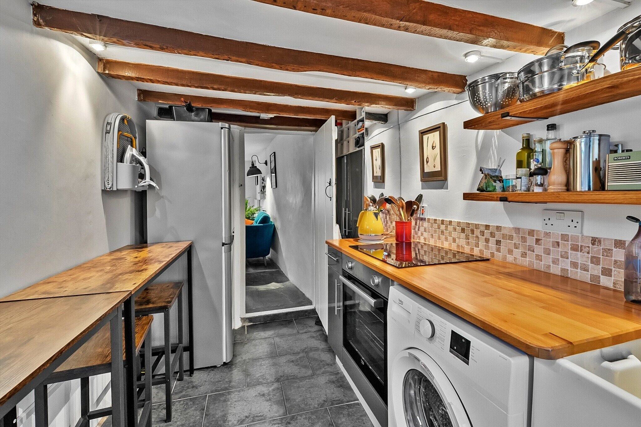 Une cuisine compacte dotée d’un plan de travail en bois, d’un lave-linge et d’un petit coin repas avec des bancs.