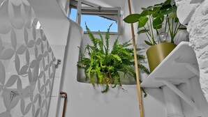 A bathroom with a window, a shower, a sink, and a potted plant.