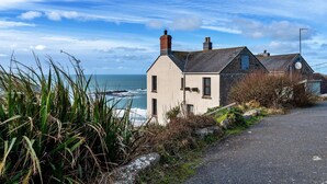 Een huis aan de kust met een stenen gevel, een schuin dak en uitzicht op zee.