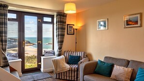 Een woonkamer met een bank, fauteuils en uitzicht op zee door grote ramen.