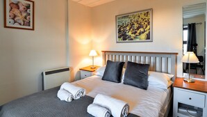 Een net opgemaakt bed met kussens, een bedlampje en een ingelijst foto aan de muur.