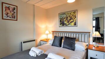 Een net opgemaakt bed met kussens, een bedlampje en een ingelijst foto aan de muur.