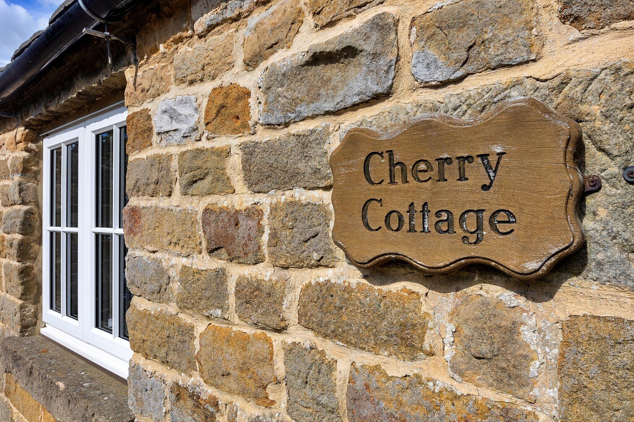Une petite maison en pierre avec une enseigne en bois sur laquelle on peut lire : « Cherry Cottage ».