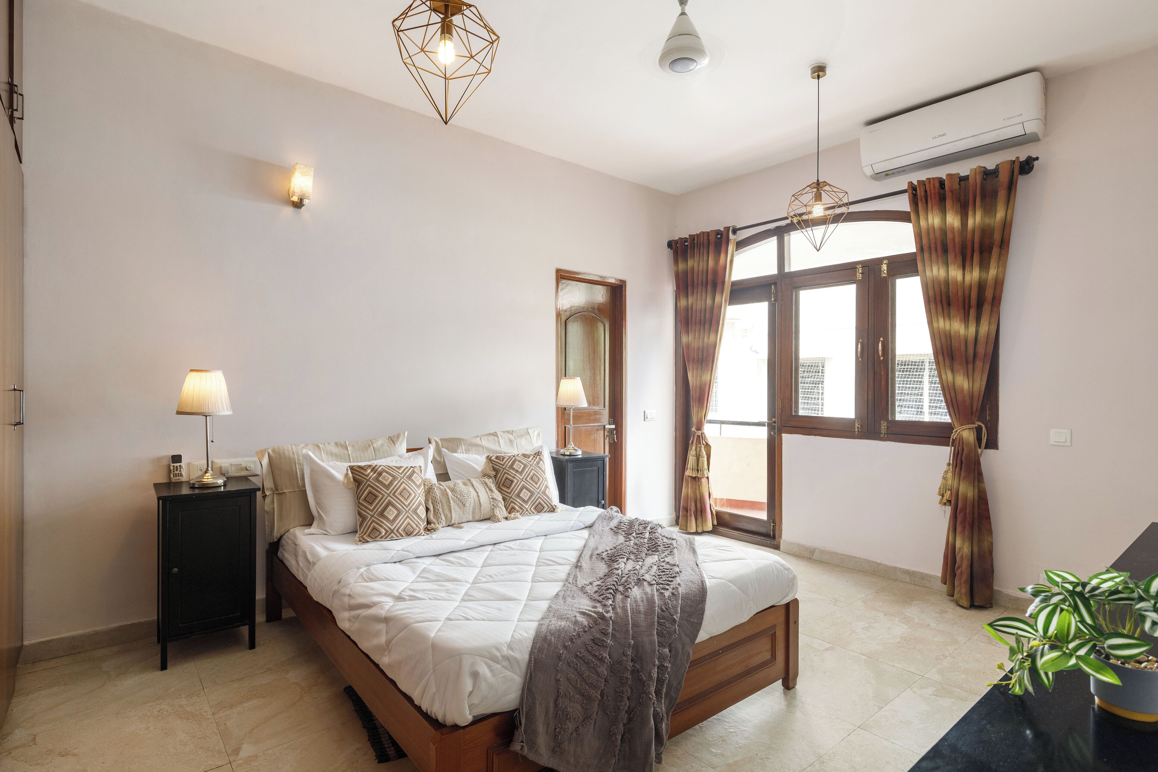 A bedroom with a bed, bedside tables, a lamp, an air conditioner, and a window with curtains.