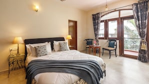 A bedroom with a bed, bedside lamps, a chair, a table, and a balcony with curtains.