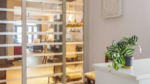 A modern interior with a sliding glass door leading to a dining area, a white counter with a potted plant, and a framed artwork on the wall.