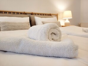 A neatly made bed with white linens and a rolled white towel.