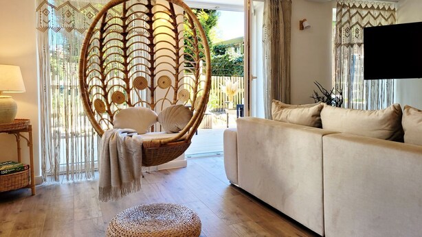 A living room with a hanging chair, a sofa, and a round ottoman. - Modern lounge apartment with terrace, beach chair, parking - 50 meters to the beach (Sierksdorf)