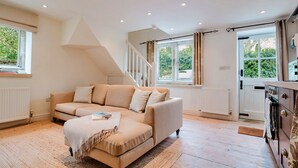 Un salon moderne avec un canapé beige, un plancher en bois et de grandes fenêtres donnant sur un paysage verdoyant.