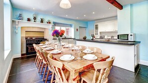 A spacious kitchen with a central island, white cabinets, and a dining area set for six with wooden chairs and a table. - Holiday home near Slapton Sands, No Deposit (Slapton)
