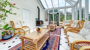 A conservatory with wicker furniture, a fireplace, and a large window. - Holiday home near Slapton Sands, No Deposit (Slapton)