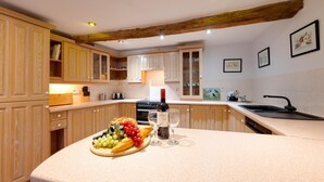 A kitchen with wooden cabinets, a countertop with a fruit platter, wine glasses, and a bottle. - Pet-friendly cottage in Slapton, No Deposit (Slapton)