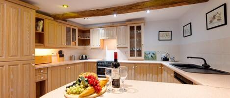 A kitchen with wooden cabinets, a countertop with a fruit platter, wine glasses, and a bottle.