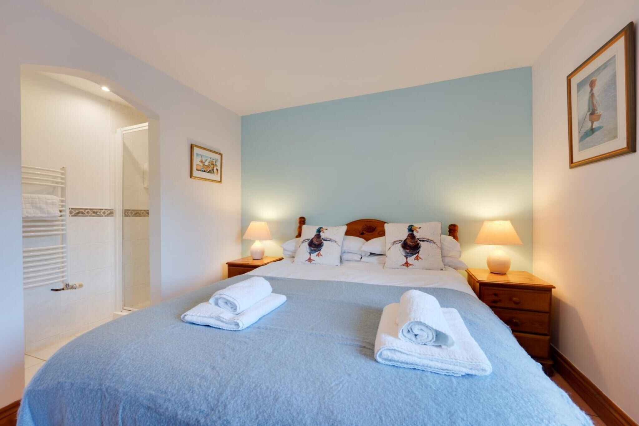 A neatly made bed with two rolled towels, a wooden headboard, and two bedside lamps.