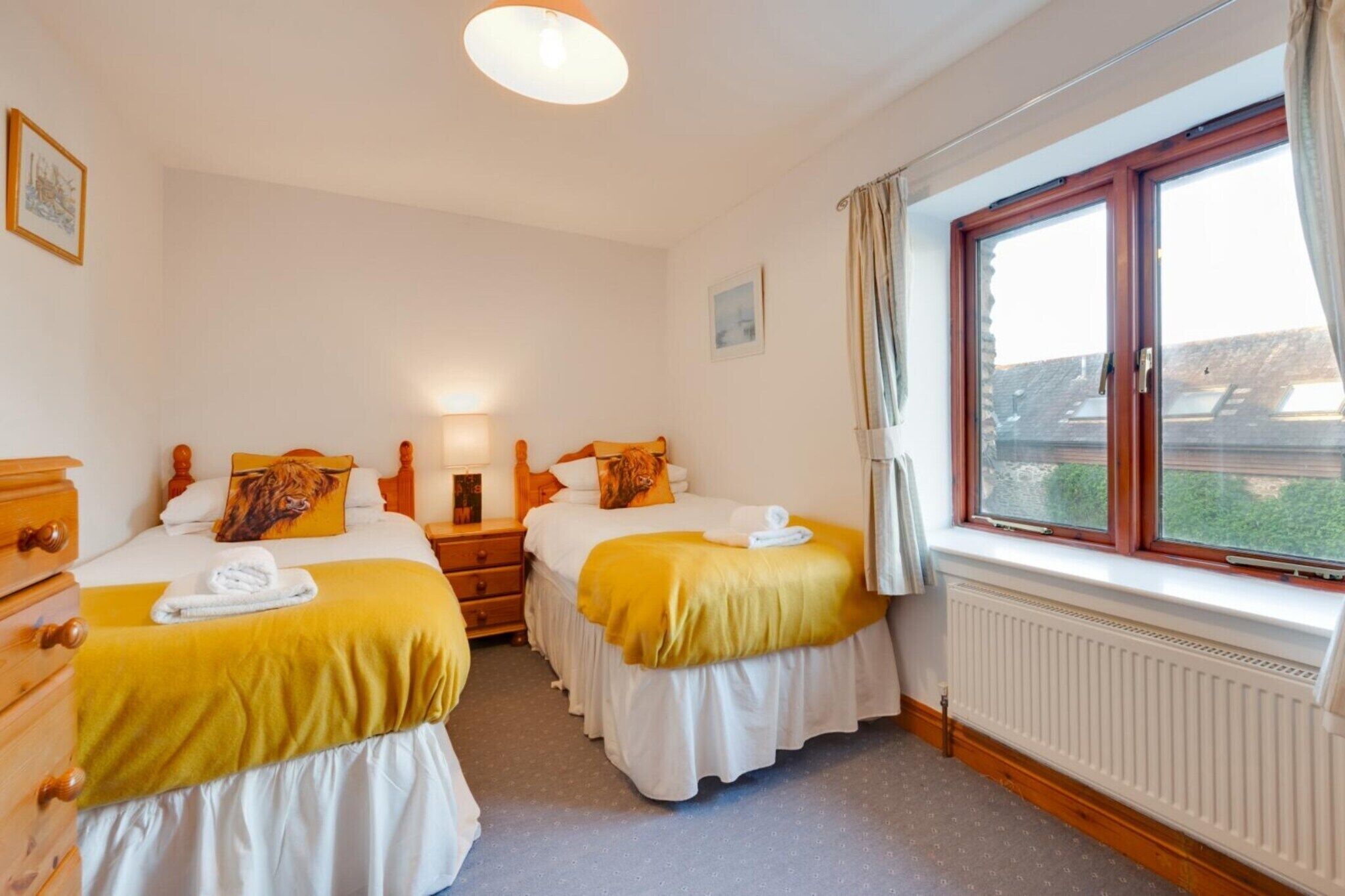 Una habitació d'hotel amb dos llits, una finestra amb cortines, un radiador i un quadre a la paret.