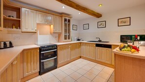 A kitchen with wooden cabinets, a stove, a microwave, and a sink. - Pet-friendly cottage in Slapton, No Deposit (Slapton)