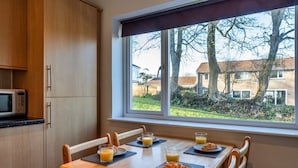 A breakfast table with plates of food and glasses of orange juice, a microwave, and a window with a view of houses and trees.
