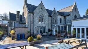 A stone building with a large arched window and a covered patio area with wooden tables and chairs.