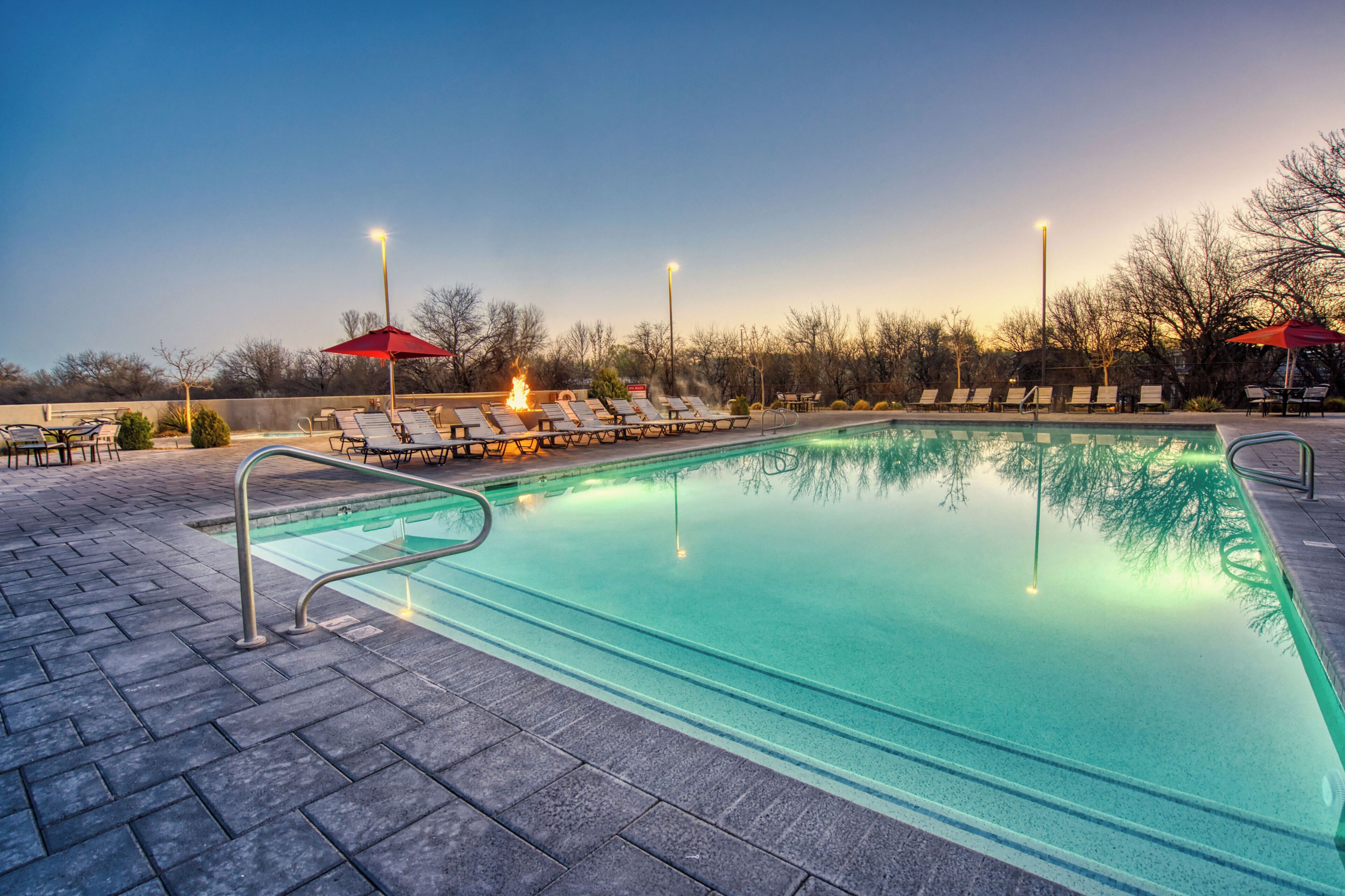 A swimming pool with lounge chairs and umbrellas, surrounded by a brick patio.