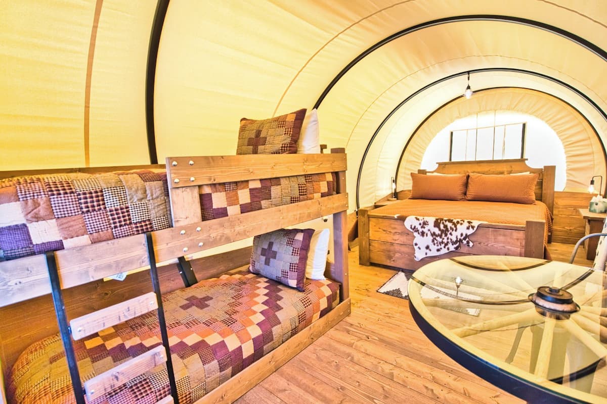 A tent with a bunk bed and a single bed, both with wooden frames and checkered bedding.