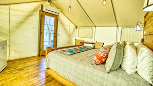 Une pièce aménagée avec une tente, un lit, un plancher en bois, une porte et une fenêtre.