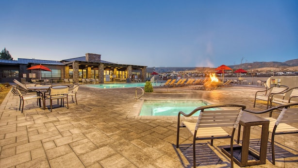 Un espace aménagé au bord de la piscine, avec des chaises longues, un foyer et un bâtiment doté de grandes fenêtres.