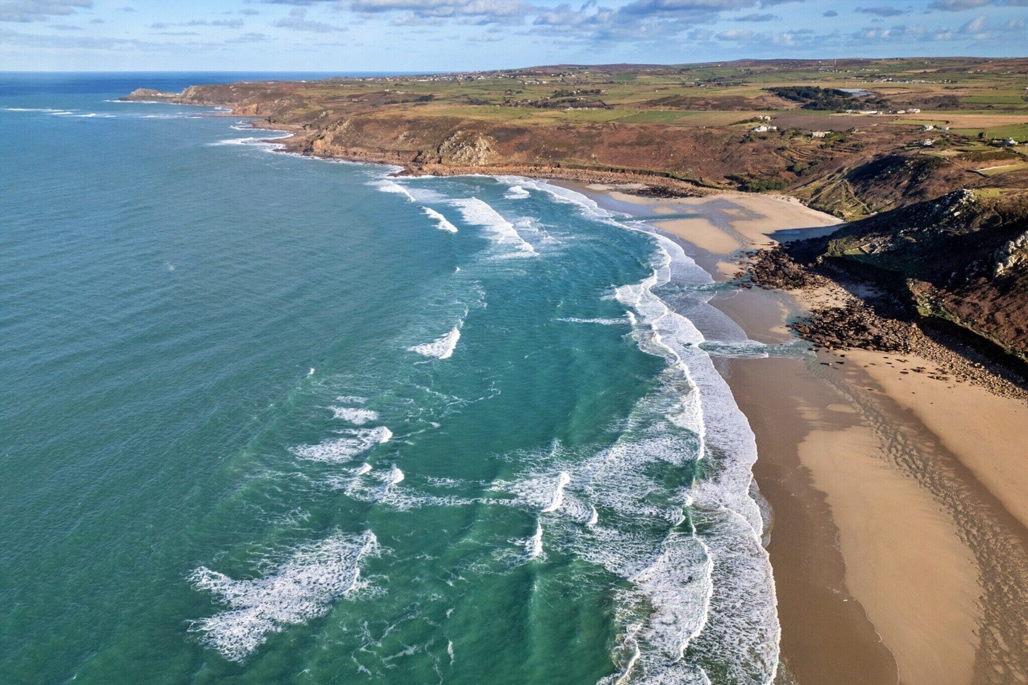 An aerial view of a coastal area with a sandy beach and rocky cliffs.