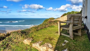 A wooden bench by a coastal path with a view of the sea and a building in the background.