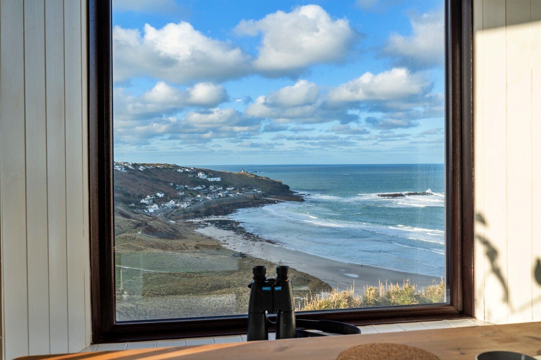 A window with a view of a coastal landscape, including a beach, ocean, and a lighthouse.