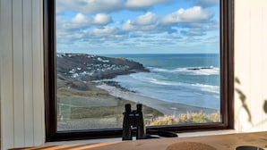 A window with a view of a coastal landscape, including a beach, ocean, and a lighthouse.