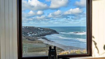 A window with a view of a coastal landscape, including a beach, ocean, and a lighthouse.
