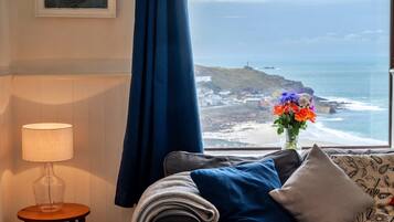 A room with a view of the ocean, a lamp, and a vase with flowers.