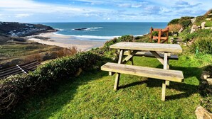 Une table de pique-nique en bois, avec des bancs, donnant sur une plage et l’océan.