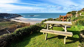 Een houten picknicktafel met bankjes met uitzicht op een strand en de oceaan.