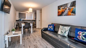 Een moderne woonkamer met een leren zwarte bank, een eettafel met stoelen, een keukenhoek en een wandgemonteerde flatscreen-tv.