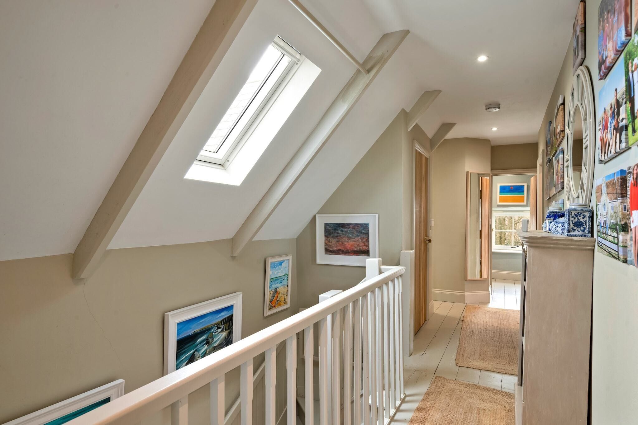 A hallway with a sloped ceiling, skylights, and a white railing.