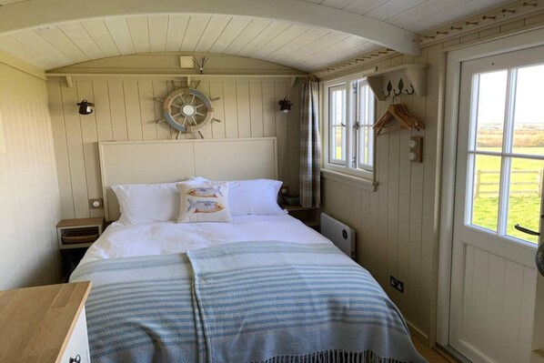 A cozy bedroom with a bed, a ship's wheel decoration, a window with a view, and a coat hanging by the door.