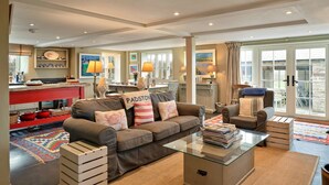 A spacious living area with a sofa, armchairs, a glass coffee table, and a red kitchen counter.