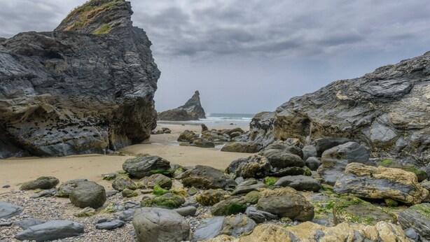 A rocky beach with large boulders and a narrow passageway leading to the sea.