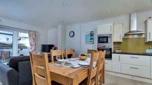 A modern kitchen with white cabinets, a built-in oven, and a microwave. There is a dining table set for four with chairs.