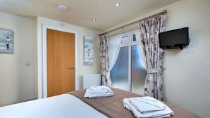 A hotel room with a bed, a television mounted on the wall, and a window with curtains.