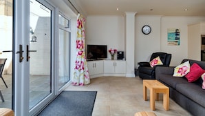 A living room with a sofa, a television, a cabinet, and a door leading to an outdoor area.
