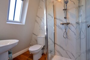 A bathroom with a marble wall, a toilet, a shower with a glass door, and a window. - Apartment in Matlock near Peak District Trails (Matlock)