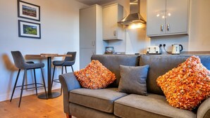 A modern living room with a grey sofa, two armchairs, a wooden coffee table, and a kitchen area with cabinets and appliances. - Apartment in Matlock near Peak District Trails (Matlock)