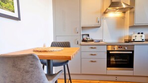 A modern kitchen with a wooden table, two chairs, a toaster, and an oven. - Apartment in Matlock near Peak District Trails (Matlock)