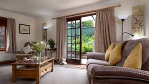 A cozy living room with a sofa, coffee table, and a view of a garden through a glass door.