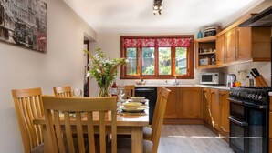 A modern kitchen with wooden cabinets, a dining table with chairs, a microwave, a stove, and a window with a red valance.