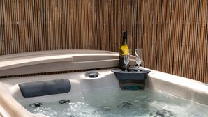 A hot tub with a bottle and glasses on the edge, surrounded by a bamboo fence.