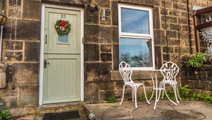 A stone building with a green door, a window, and a white table with chairs.